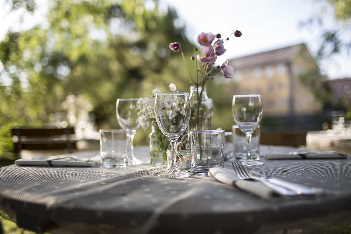 Ett bord dukat med glas, bestick och blommor utomhus